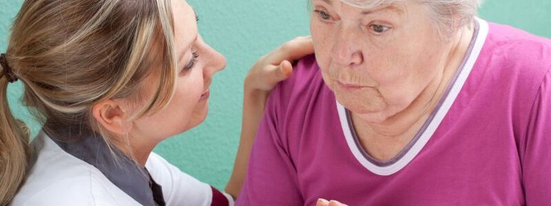 A young nurse holds the hand of an elderly woman