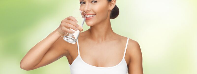 Hübsche Frau mit gesundem Essen vor sich und einem Glas Wasser in der Hand