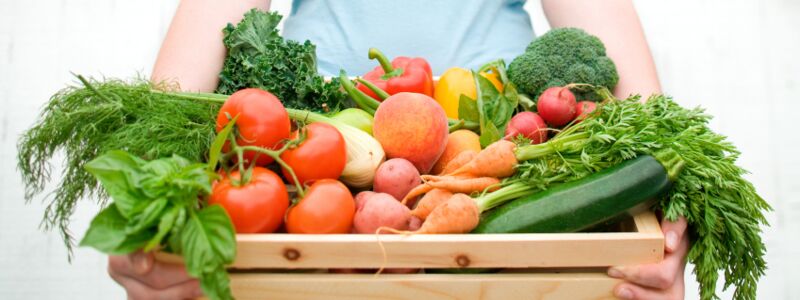 Frau trägt eine Kiste mit frischem Obst und Gemüse