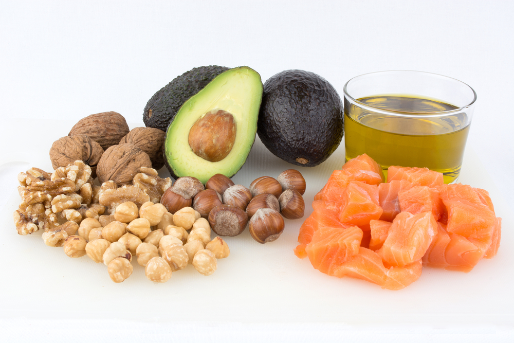 Nuts, avocado, a glass of olive oil and raw salmon side by side.