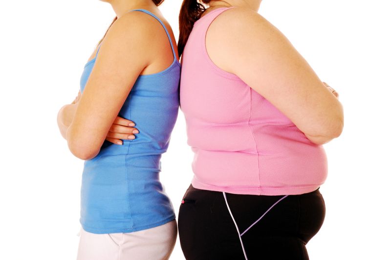 An overweight and a slender woman stand back to back in sportswear