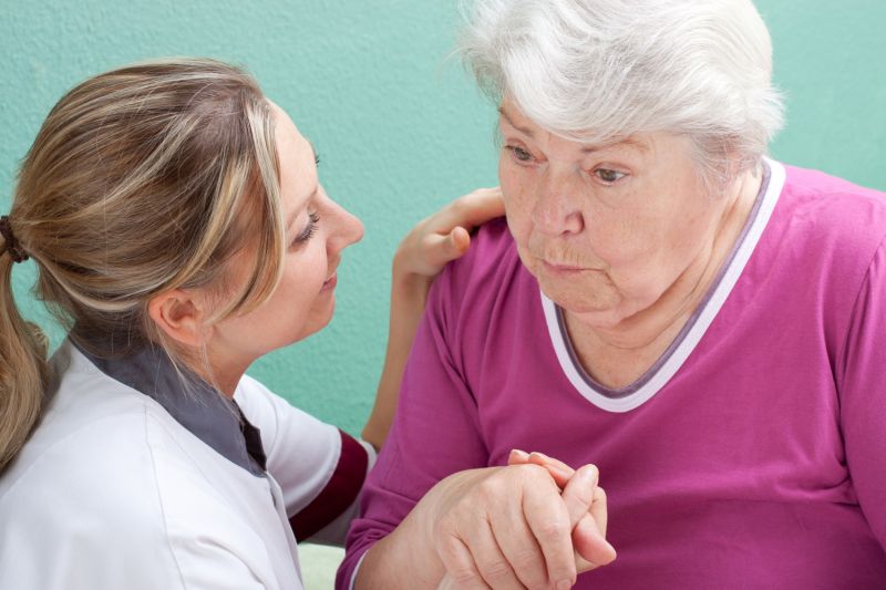 A young nurse holds the hand of an elderly woman