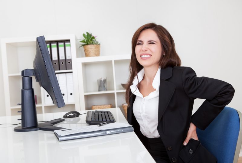 Woman at a desk holds back in pain